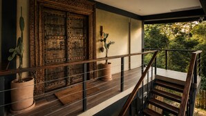 A wooden staircase leading to a balcony with a view of greenery.