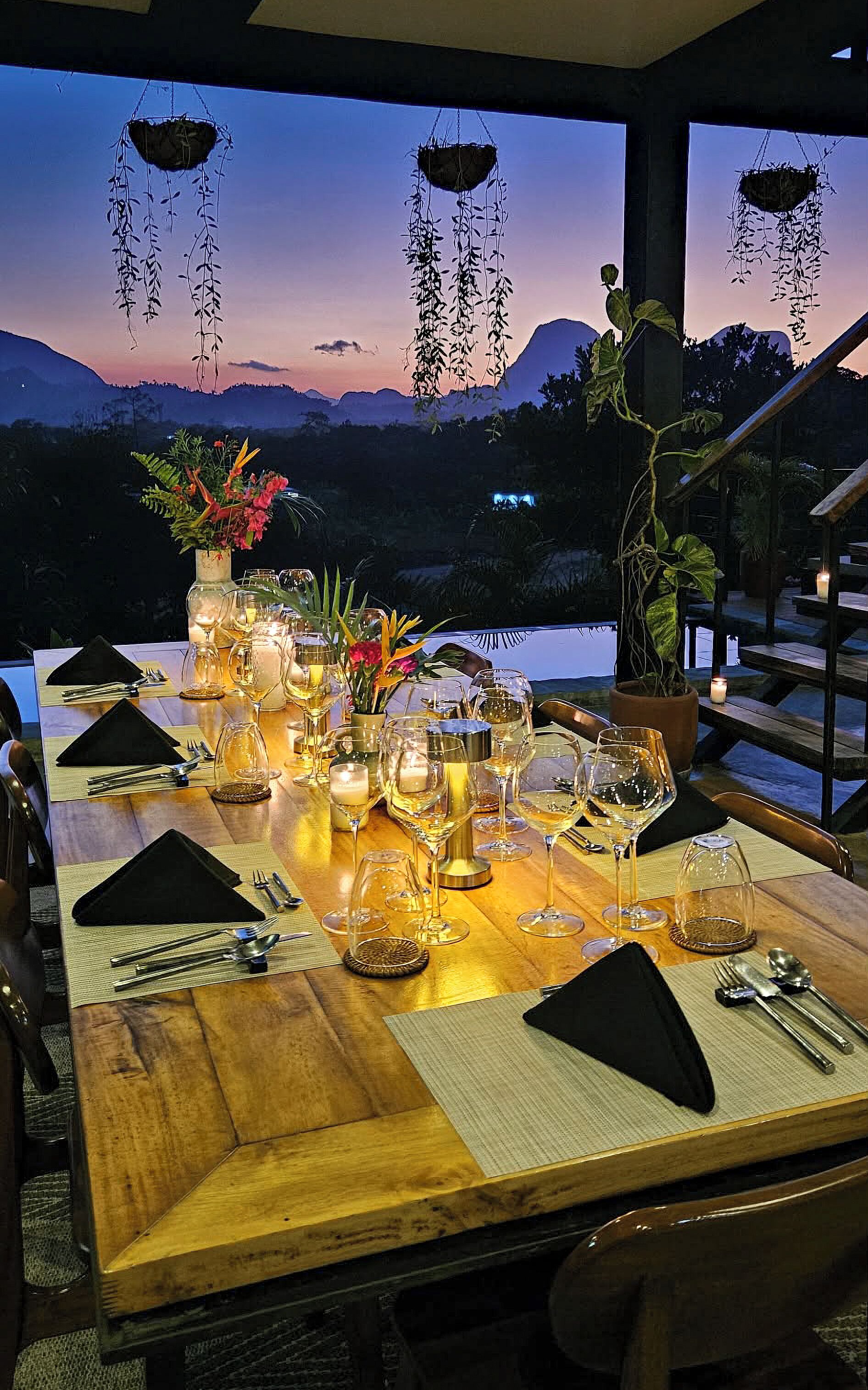 A dining table set for a meal with a view of mountains and a sunset.