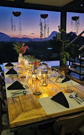 A dining table set for a meal with a view of mountains and a sunset.