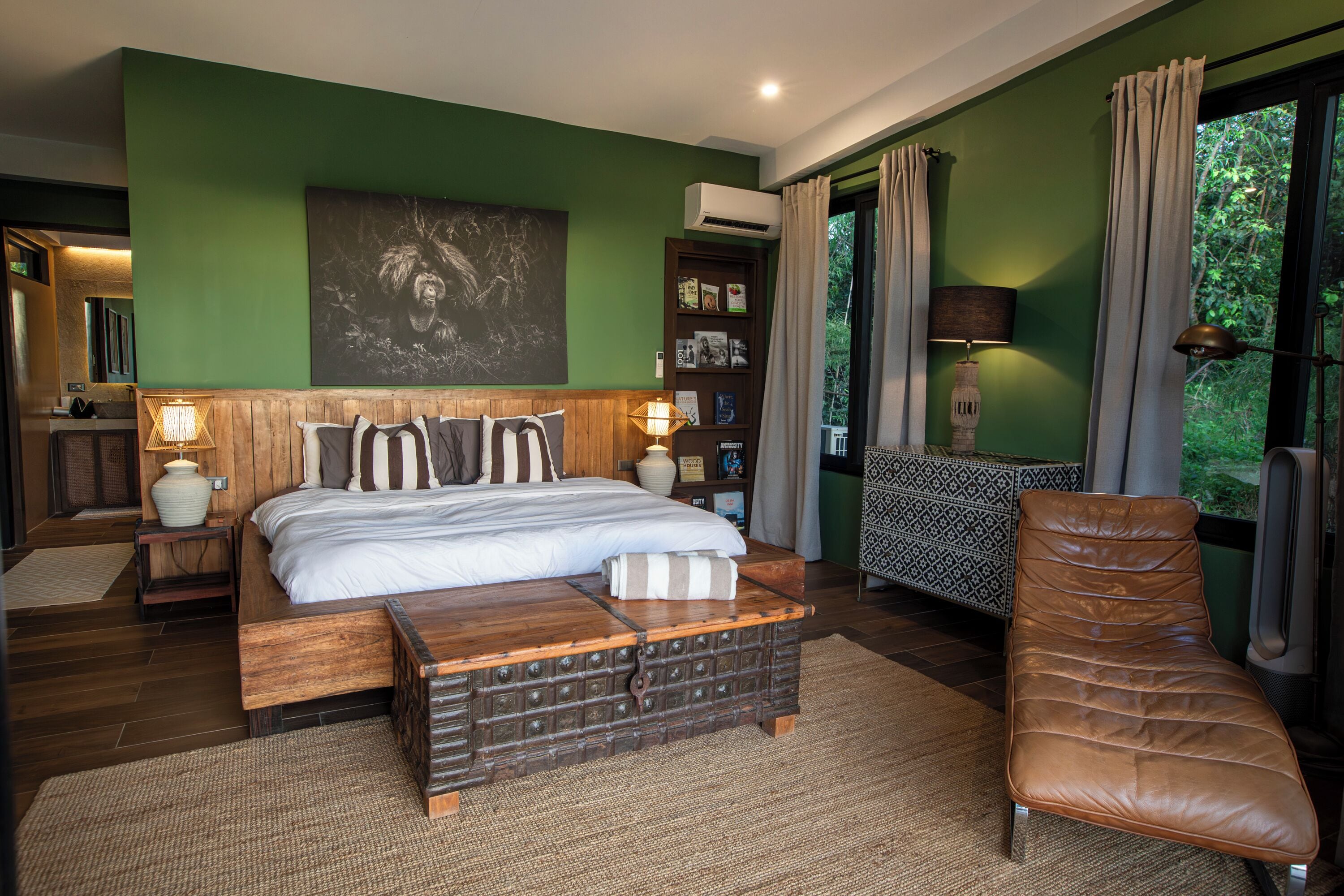 A bedroom with a bed, bedside tables, a reading chair, and a large window with curtains.