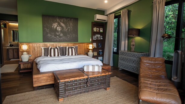 A bedroom with a bed, bedside tables, a reading chair, and a large window with curtains.
