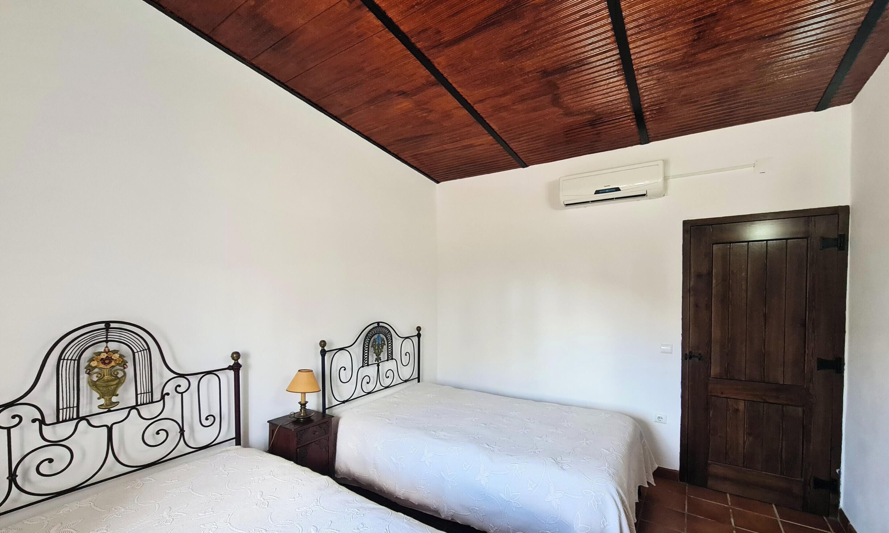 A bedroom with two beds, a wooden ceiling, a door, and an air conditioning unit.