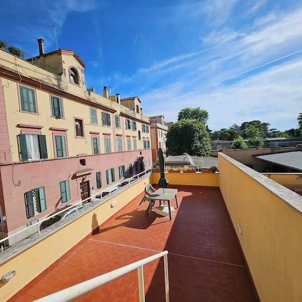 Une terrasse sur le toit offrant une vue sur les bâtiments adjacents, avec une rambarde et une table entourée de chaises.