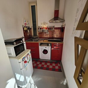 A compact kitchen with a microwave, washing machine, and red cabinetry. - A charming, stylish open-concept space (Roma)