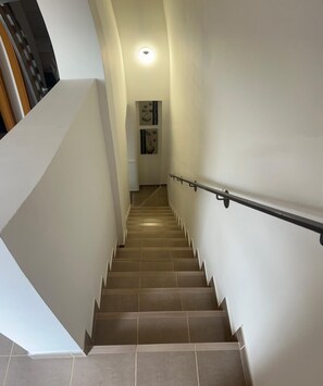 Un escalier avec une rampe, des murs blancs et un luminaire au plafond.