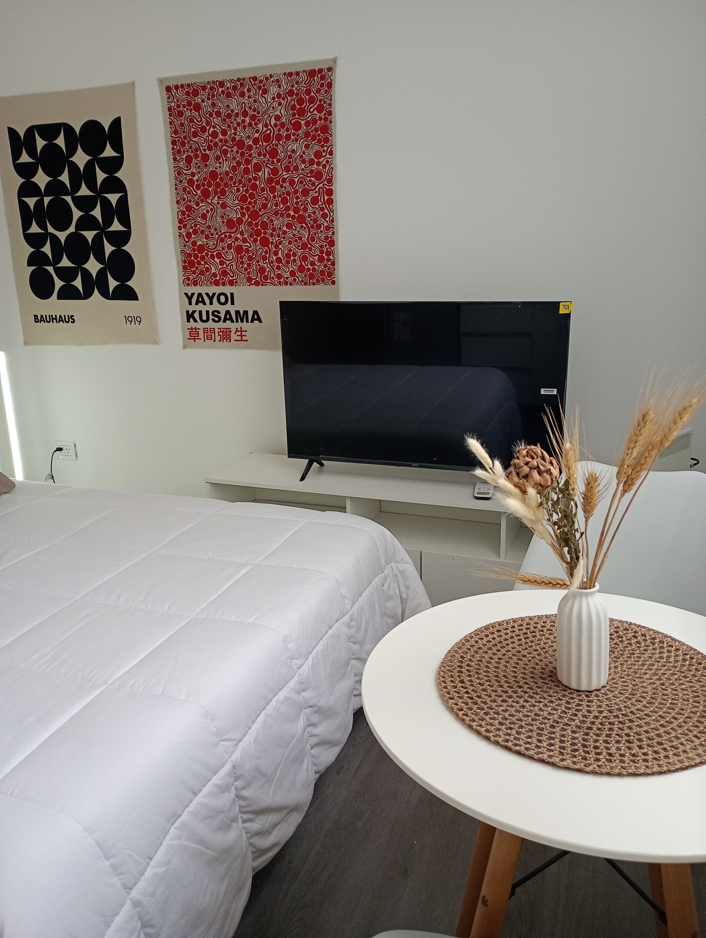 Ein Hotelzimmer mit einem Bett, einem Fernseher auf einem Schrank, einem kleinen runden Tisch mit einer Vase und zwei Wandbildern.