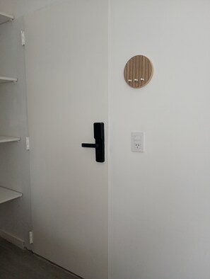 A white door with a black handle, a white electrical outlet, and a wooden wall-mounted object. - Acogedor departamento en Villa Urquiza (Buenos Aires)