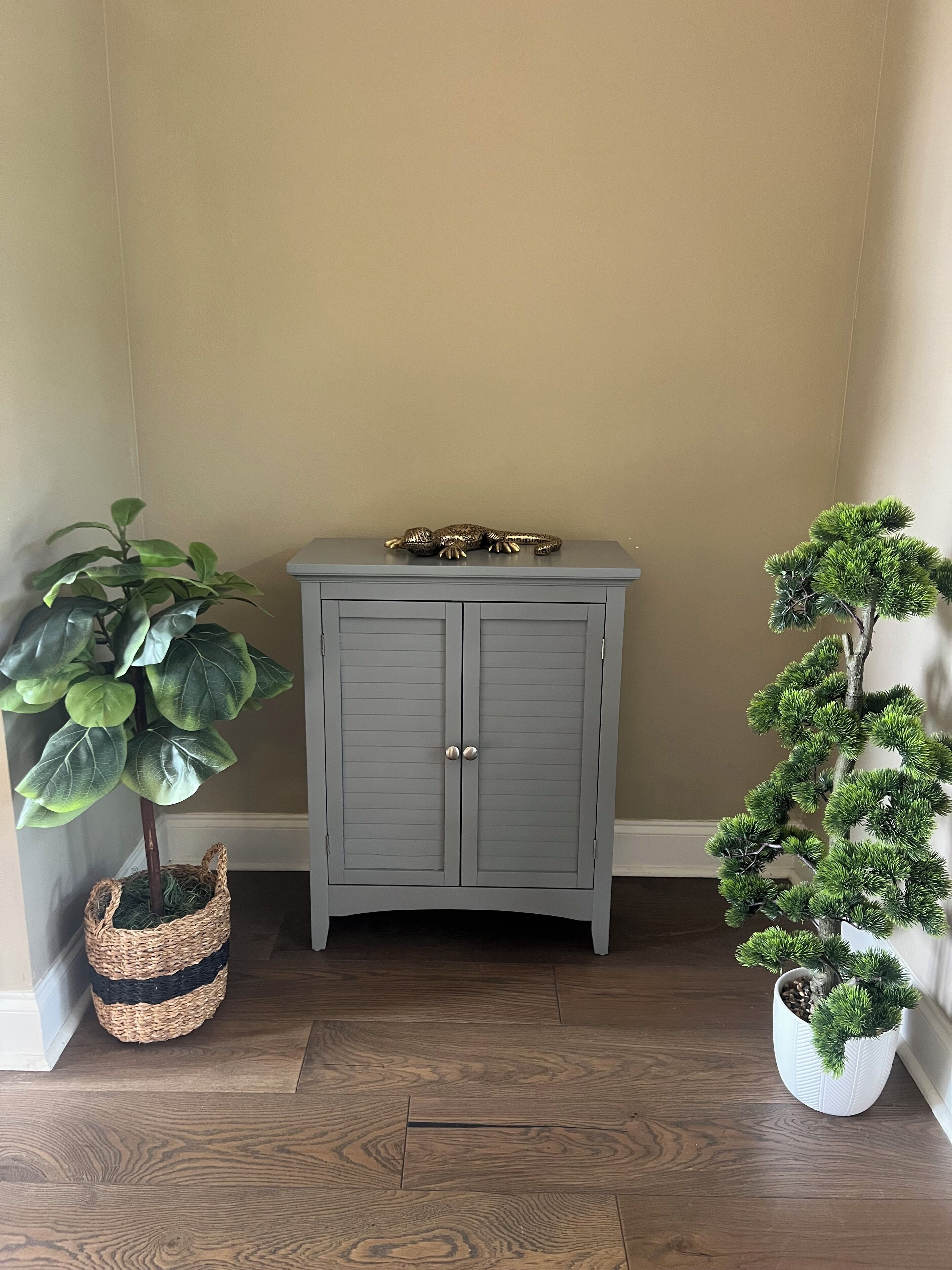 Eine Zimmerecke mit einem grauen Schrank, einem Blumentopf und einer Bonsai-Pflanze.
