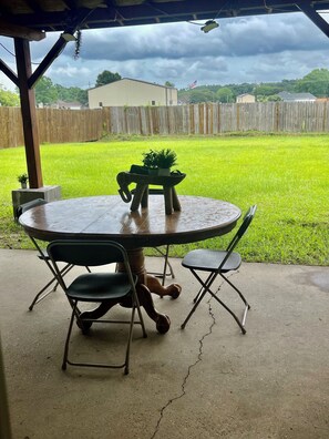 A patio with a round table and chairs, a small potted plant, and a view of a grassy yard and a wooden fence. - 3-bedroom house in nice Gonzales with cool AC comfort (Gonzales)