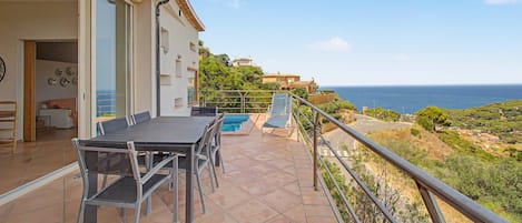 A balcony with a dining table and chairs, a pool, and a view of the sea.