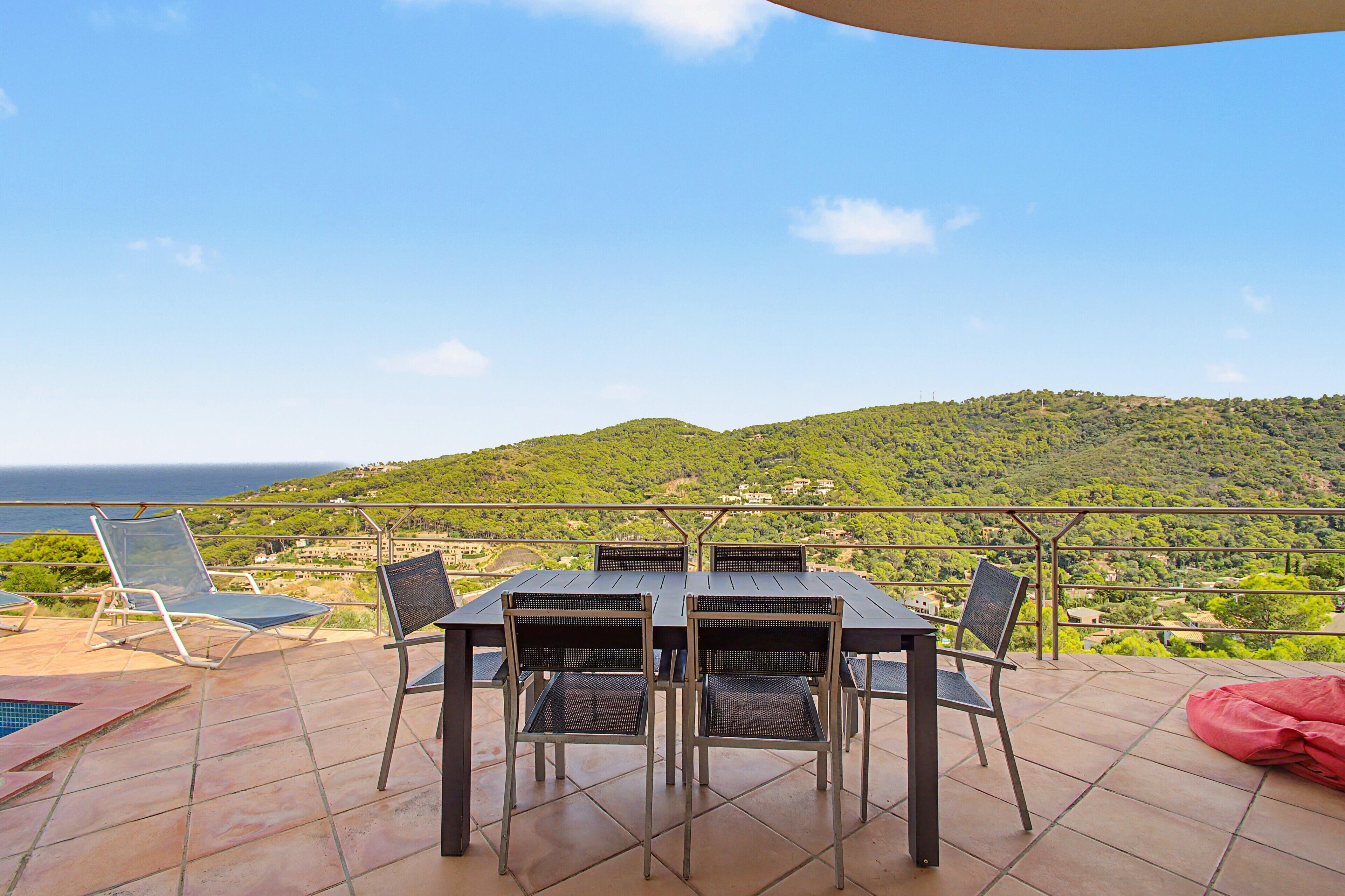 Une terrasse avec une table et des chaises, offrant une vue sur une colline et la mer.