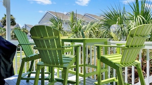 En terrass med gröna Adirondack-stolar och ett vitt räcke, med utsikt över ett bostadsområde med hus och palmer.