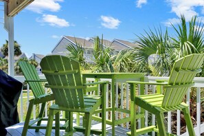 Eine Terrasse mit grünen Adirondack-Stühlen und einer weißen Geländer, mit Blick auf eine Wohngegend mit Häusern und Palmen.
