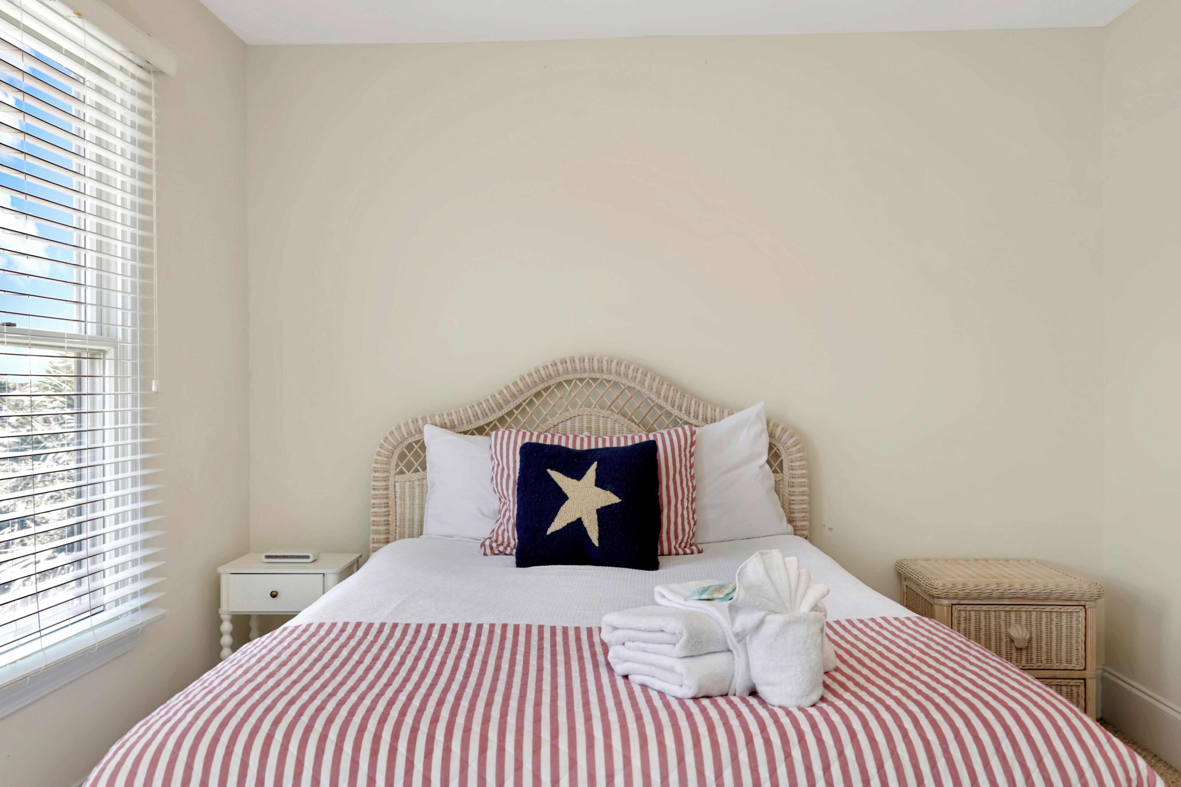 A neatly made bed with striped bedding, a star pillow, and a small bedside table with a lamp.