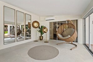 Ein modernes Interieur mit einem großen Spiegel, einem Rattan-Sessel, einer Stehlampe und einer Topfpflanze.