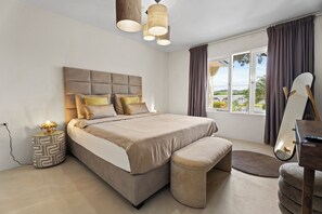Ein modernes Schlafzimmer mit einem großen Bett, Nachttischlampen, einem Beistelltisch und Blick ins Freie.