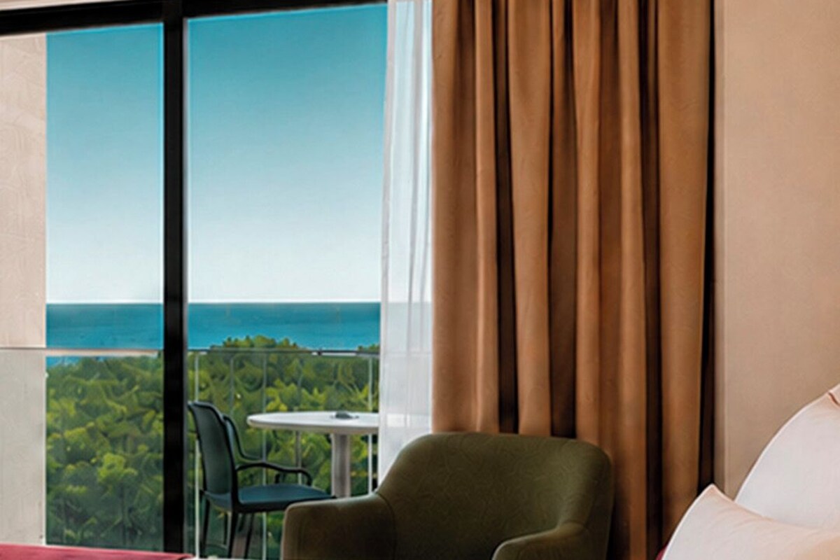 A hotel room with a large bed, a green chair, a small table, and a view of the ocean.