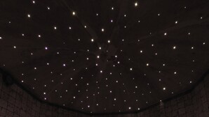 A room with a curved seating area, a patterned wall, and a ceiling with star-like lights. - Steinbock B&B (Livigno)