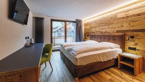 A hotel room with a bed, a desk, a chair, a television, and a window with curtains. - Steinbock B&B (Livigno)