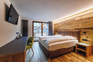 A hotel room with a bed, a desk, a chair, a television, and a window with curtains. - Steinbock B&B (Livigno)