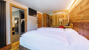 A bedroom with a bed, a television, a wooden wardrobe, and a desk with a chair. - Steinbock B&B (Livigno)