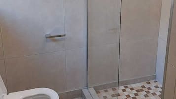 Un baño con inodoro, ducha con puerta de vidrio y suelo a cuadros.