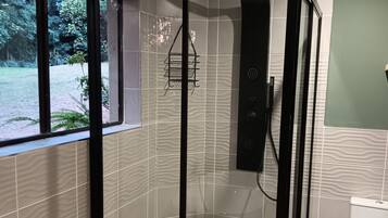 Cabina de ducha con puerta de vidrio, toallero y un inodoro a la derecha.
