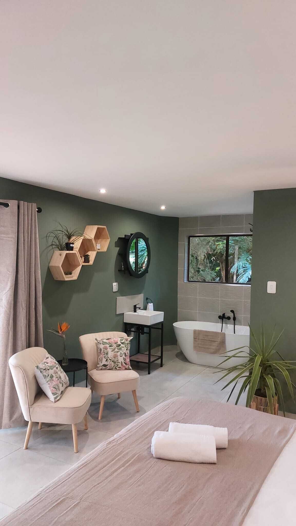Ein modernes Badezimmer mit einer Badewanne, einem Waschbecken und einem Spiegel. Zwei Stühle und ein kleiner Tisch mit einer Pflanze sind ebenfalls vorhanden.