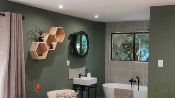 Un baño moderno con bañera, lavamanos y espejo. Hay dos sillas y una mesita con una planta.