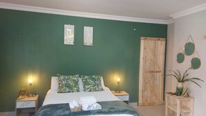 A bedroom with a bed, two bedside lamps, a wooden wardrobe, and a small table with a plant. - Guesthouse Charis  (Pretoria)