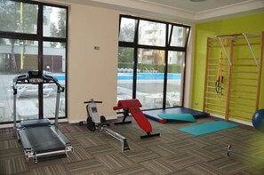 A gym with exercise equipment, large windows, and a view of a swimming pool. - Green Dream Polanki - Sauna & Bicycle & Bicycle (Kołobrzeg)