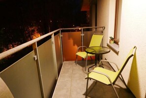A balcony with a glass table and two chairs, a window with a plant, and a view of the night sky. - Green Dream Polanki - Sauna & Bicycle & Bicycle (Kołobrzeg)