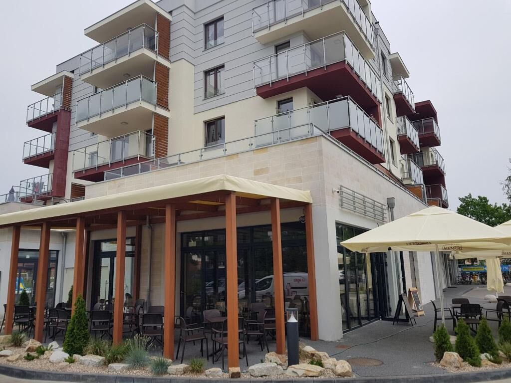 Un edificio de varios pisos con balcones, una zona de estar techada al aire libre y la entrada a un restaurante.
