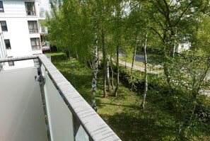 Ein Wohngebäude mit einem Balkon mit Blick auf eine begrünte Fläche mit Bäumen.