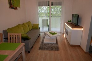 Ein Wohnzimmer mit Sofa, Couchtisch, Fernseher auf einem Schrank und einer Schiebetür zu einem Außenbereich.