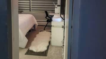 Un dormitorio con una cama, un escritorio, una silla, un televisor y una ventana con persianas.