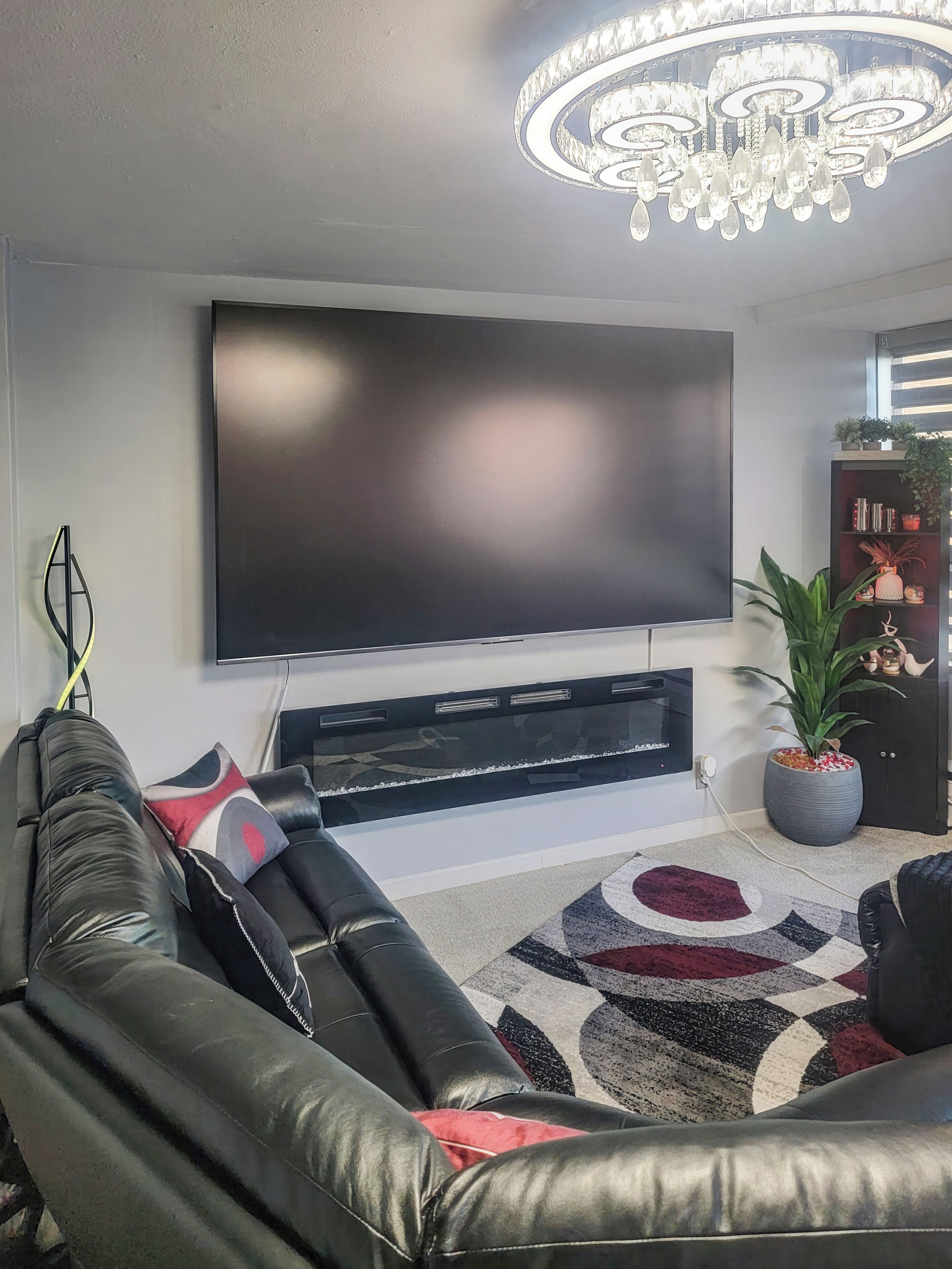 Un salon moderne avec un téléviseur à écran plat, un canapé en cuir, un tapis à motifs, un lustre et une plante en pot.