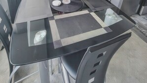 A dining table with a glass top, surrounded by chairs, a vase with flowers, and a modern abstract painting on the wall. - The River Condos (Detroit)