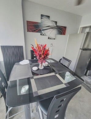 A dining table with a glass top, surrounded by chairs, a vase with flowers, and a modern abstract painting on the wall. - The River Condos (Detroit)