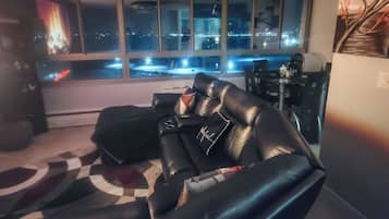 Un salón moderno con sofá de cuero negro, una araña y vista a una ciudad iluminada de noche.