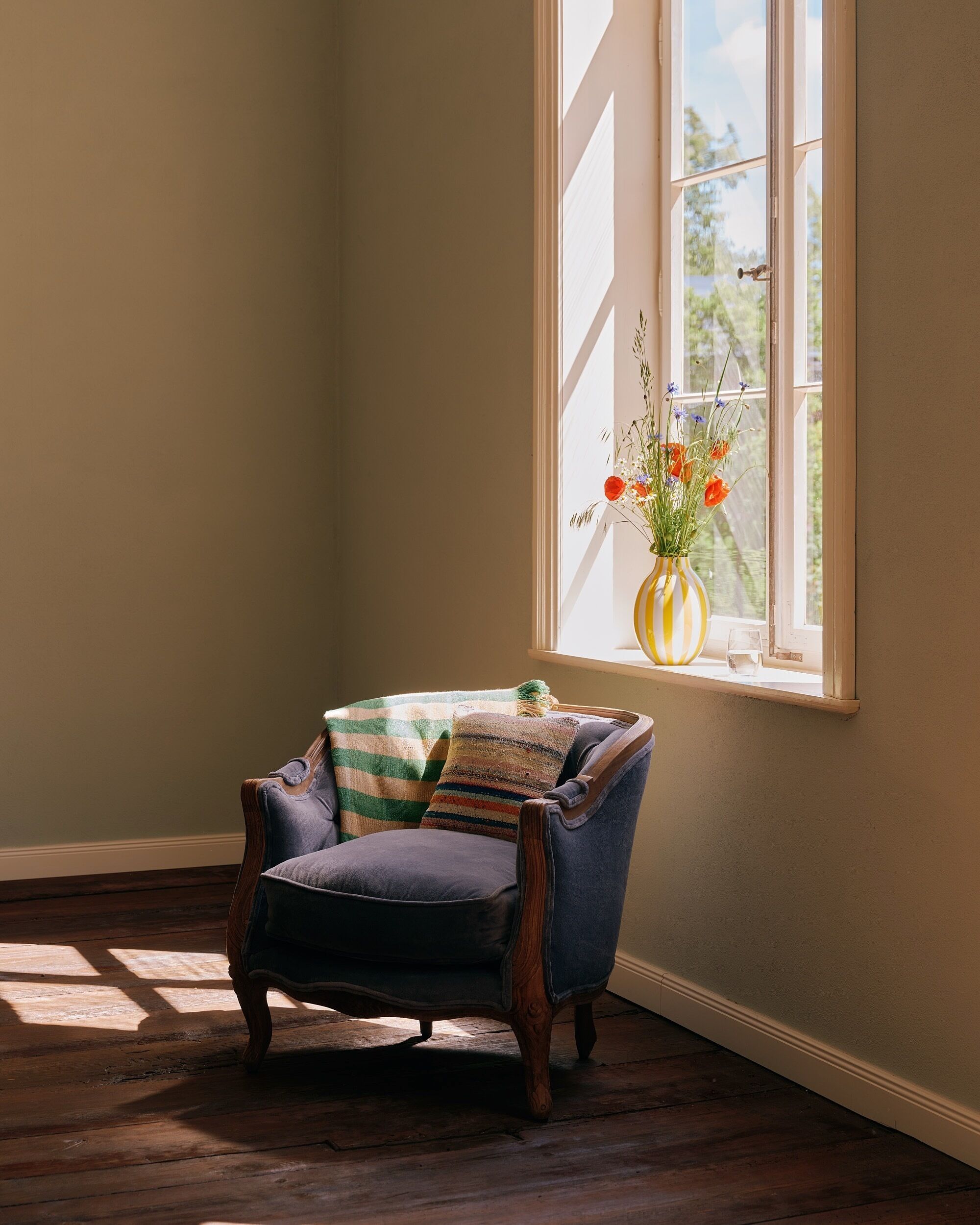 A chair with a striped cushion and a vase with flowers on a windowsill.