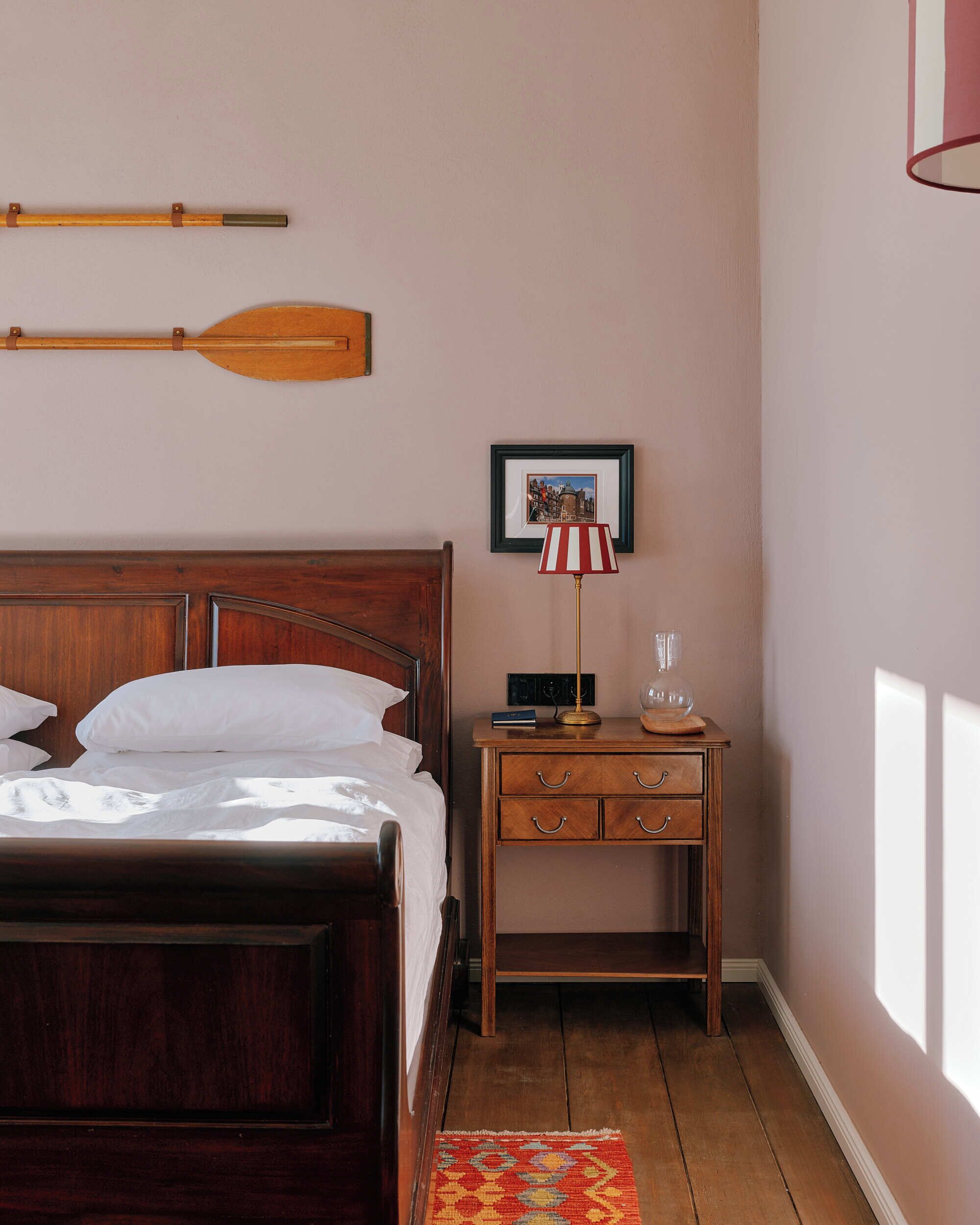 Ein Schlafzimmer mit einem hölzernen Bett, einem Nachttisch mit Lampe, einem gerahmten Bild an der Wand und einem Holzboden.
