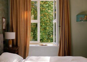 Una habitación con cama, mesita de noche, lámpara y ventana con cortinas.