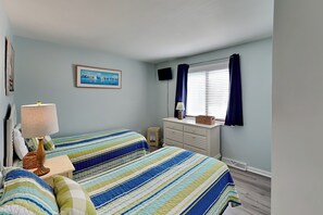 Ein Schlafzimmer mit zwei Betten, einem Schminktisch, einem Fernseher und einem Fenster mit Vorhängen.