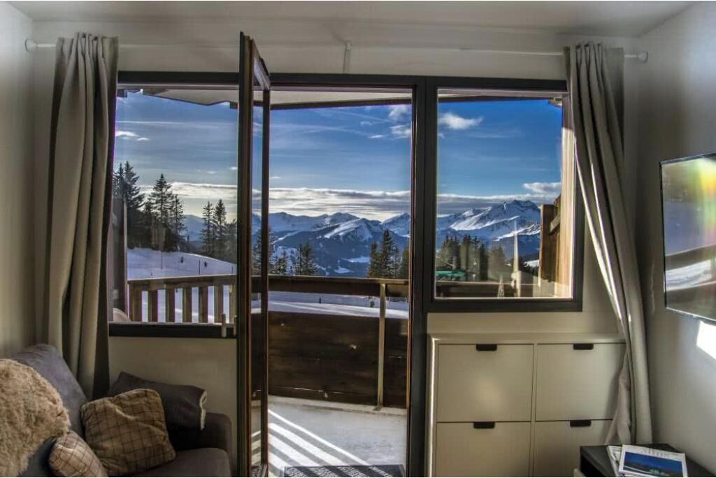 Une pièce dotée d’une grande fenêtre donnant sur les montagnes, d’une terrasse en bois à l’extérieur et d’un canapé agrémenté de coussins.