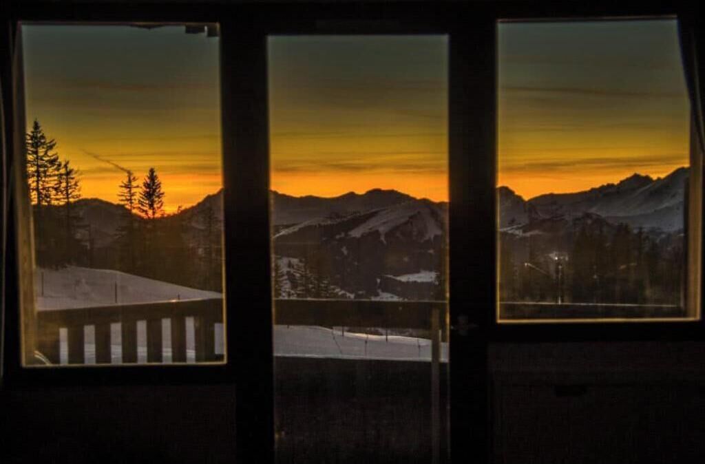 Uitzicht door een raam op een berglandschap tijdens de zonsondergang.