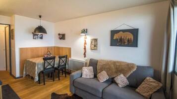 A cozy living area with a sofa, a dining table with chairs, a pendant light, and wall art.