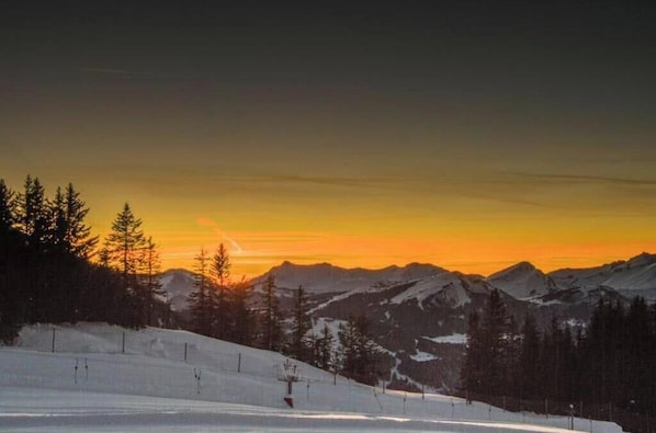 A snowy mountain landscape with a ski lift and trees during sunset.