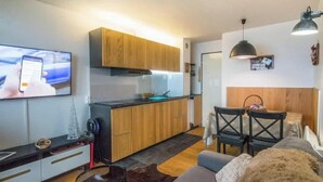 Un espacio habitable moderno con cocina, comedor y televisor de pantalla plana montado en la pared.