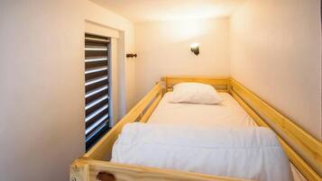 Une petite chambre avec un lit simple, un cadre en bois, un matelas blanc et un luminaire fixé au mur.
